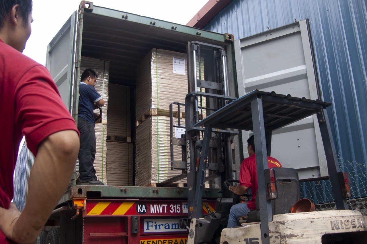 A forklift loading stacks of finished cartons into a container on a truck