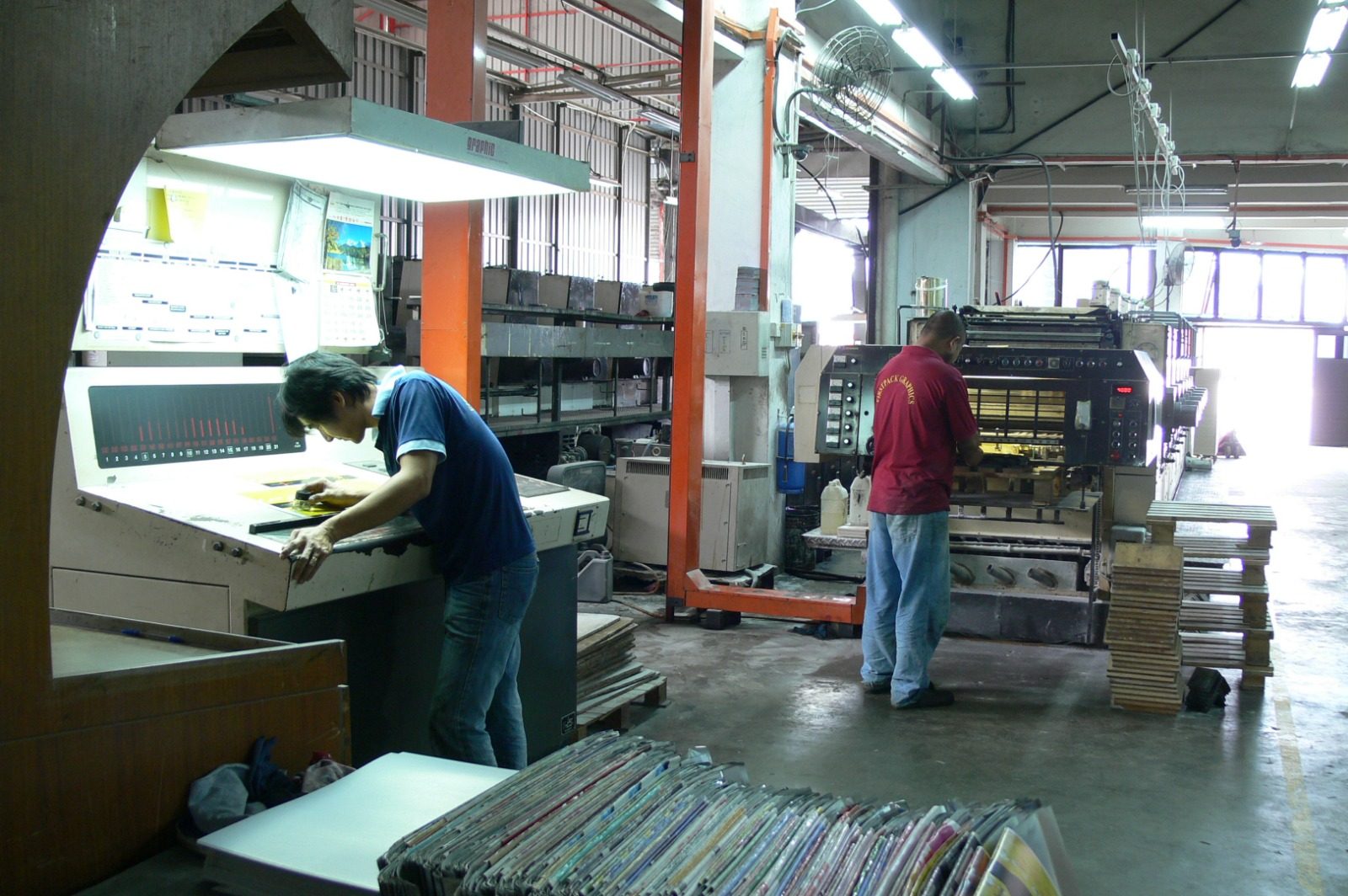 Two FirstPack operators at work — one reading a sheet at the inspection desk, one at the press units